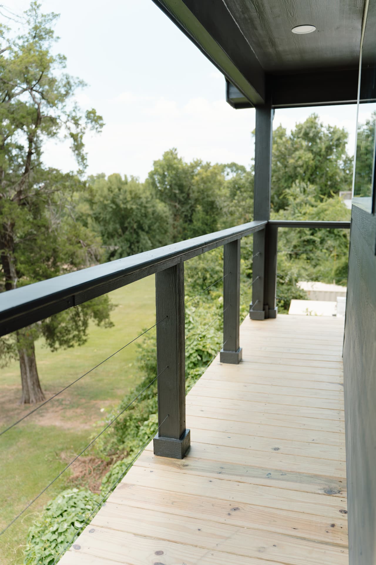 Covered upper balcony with cable railing overlooking trees